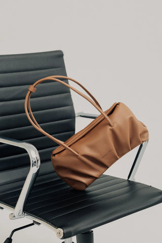 Imagen del Bolso Leonor Camel de Valentina Rivera Madrid, sobre una silla negra de oficina